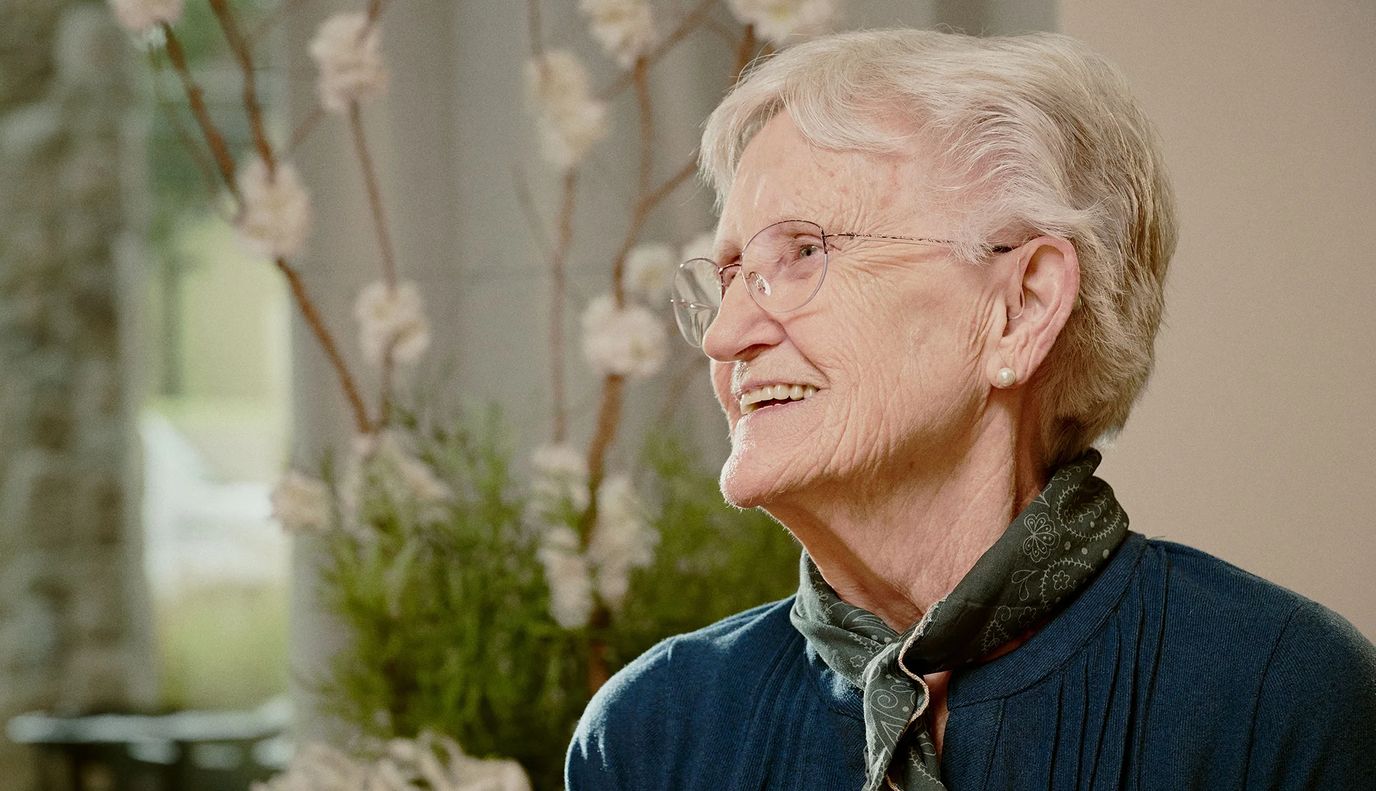 Smiling elderly woman with glasses in a cozy setting.