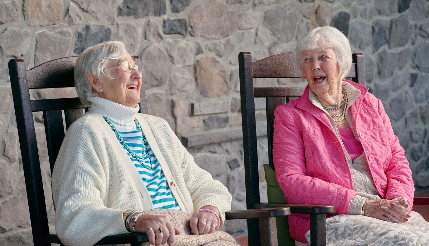 Two elderly women laughing in rocking chairs.