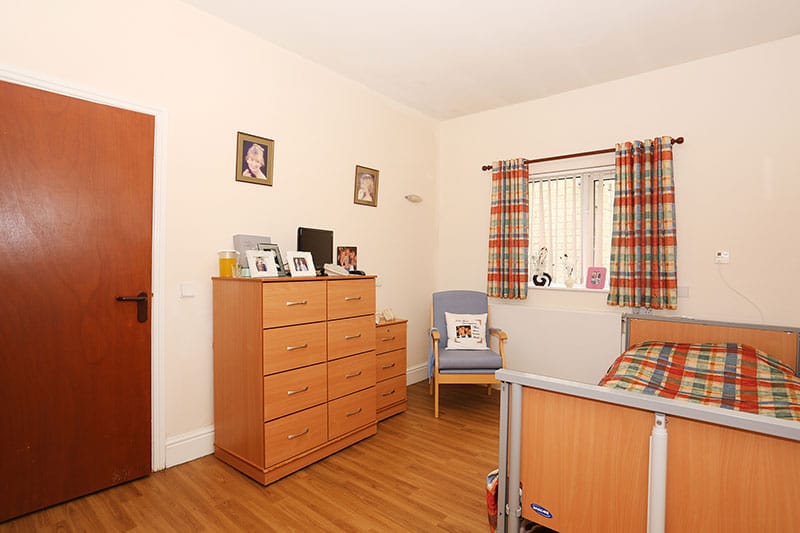 A bedroom in Lister and Sherrington House featuring a bed, bedside drawer, and comfortable chair.