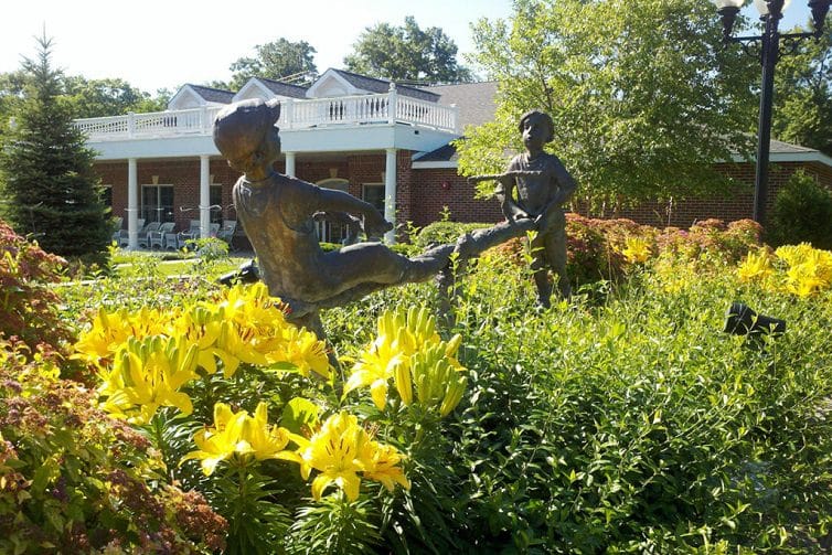 Bronze sculptures of children playing in a garden filled with yellow flowers