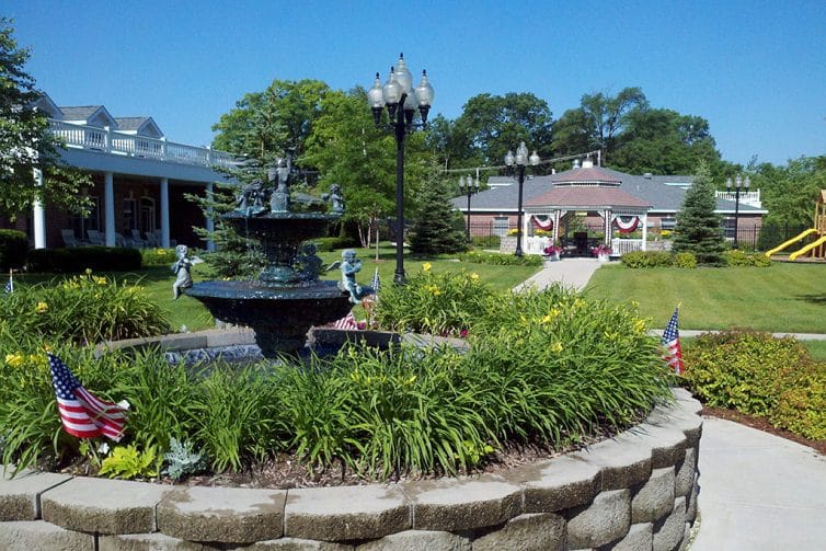 A decorative fountain surrounded by flowers and American flags at a senior living facility.