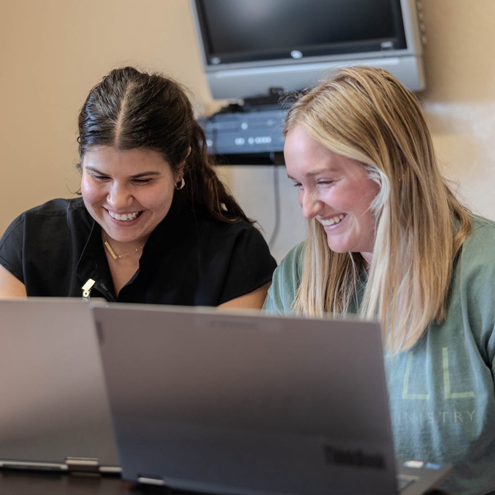 Two women smiling while working on laptops together