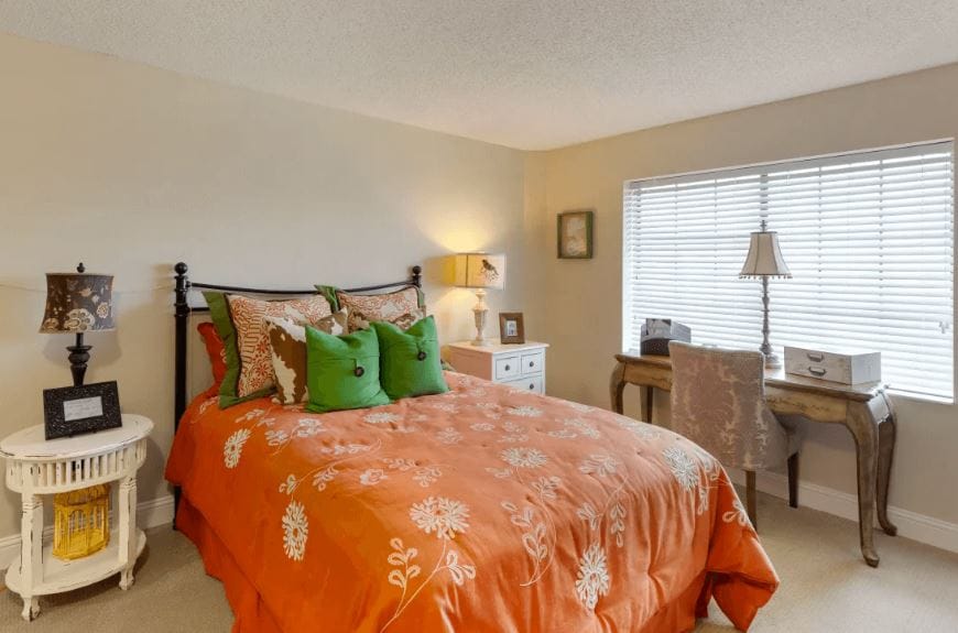 Well-decorated bedroom with orange bedding and natural light from a window.