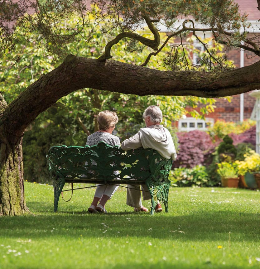 Two residents enjoying a garden bench under a tree