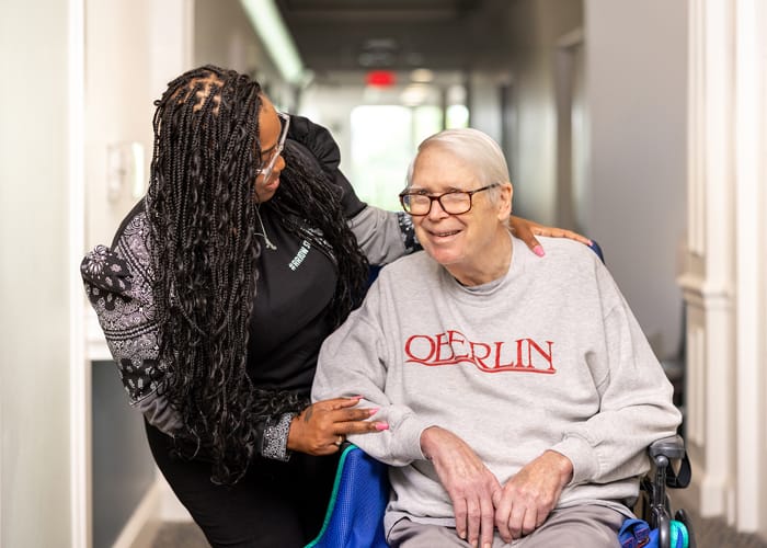 A staff member assisting a smiling resident in a long hallway