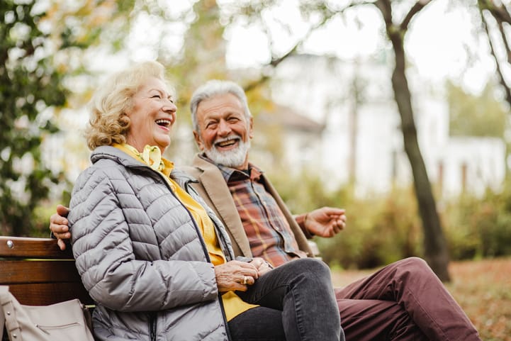 Senior couple laughing together on a bench in a garden