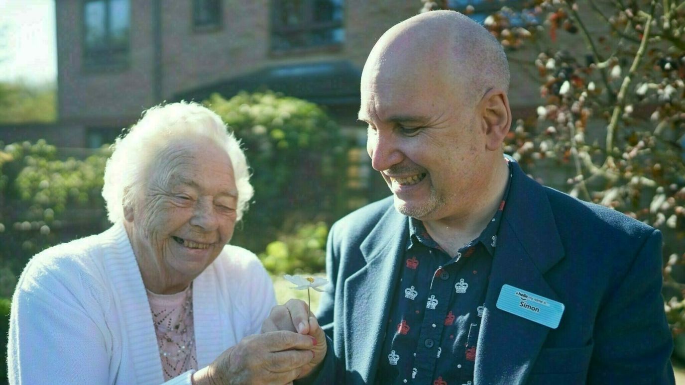 Senior resident and staff member smiling outdoors.