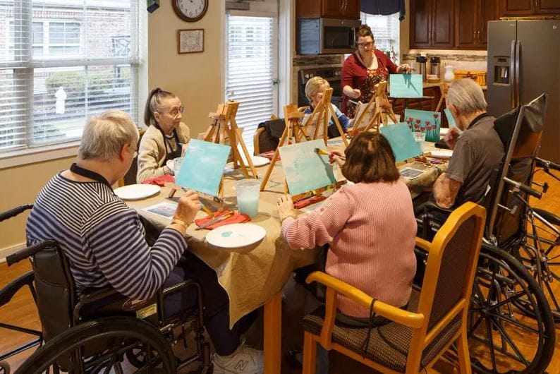 Residents painting during an art class in a dining area.