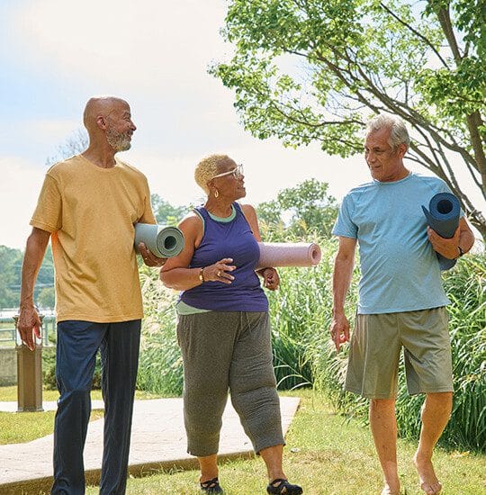 Three seniors walking outdoors with yoga mats