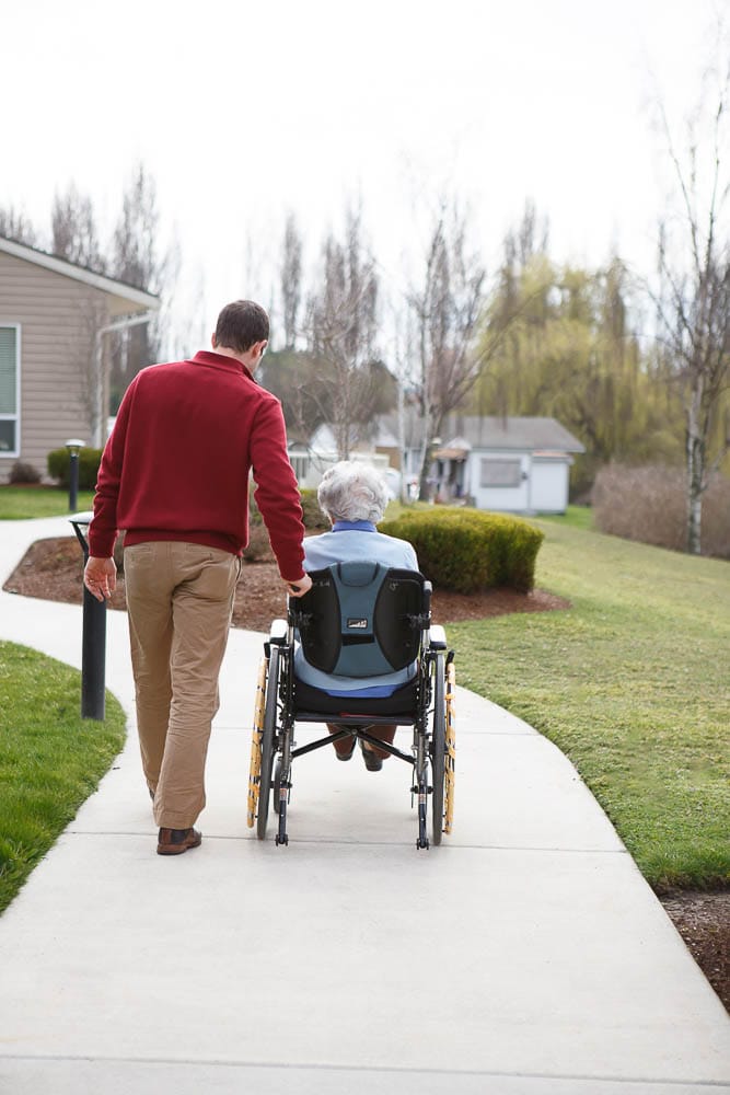 A staff member assisting a resident in a wheelchair outdoors
