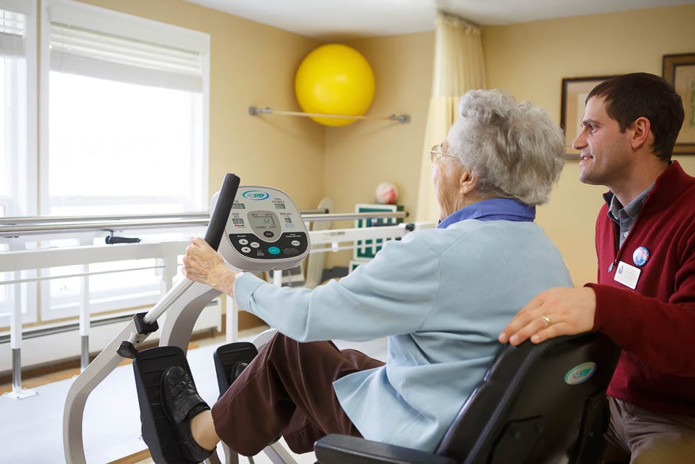A resident using exercise equipment with staff assistance