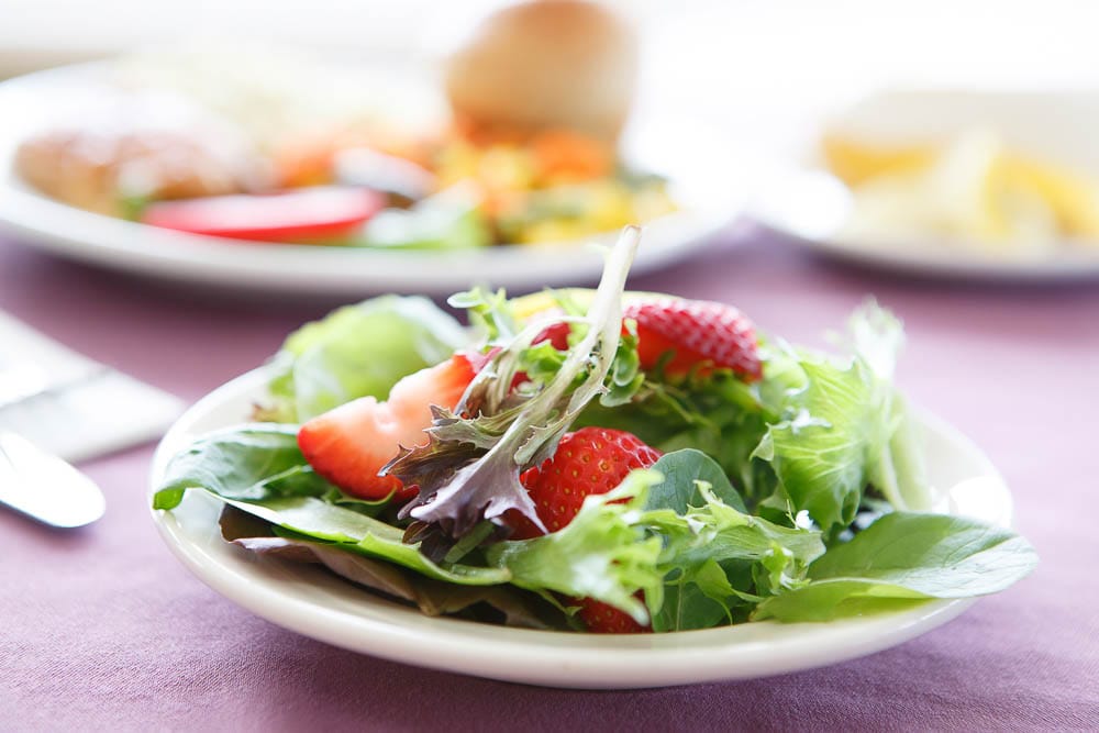 A plate of salad with strawberries in a dining setting