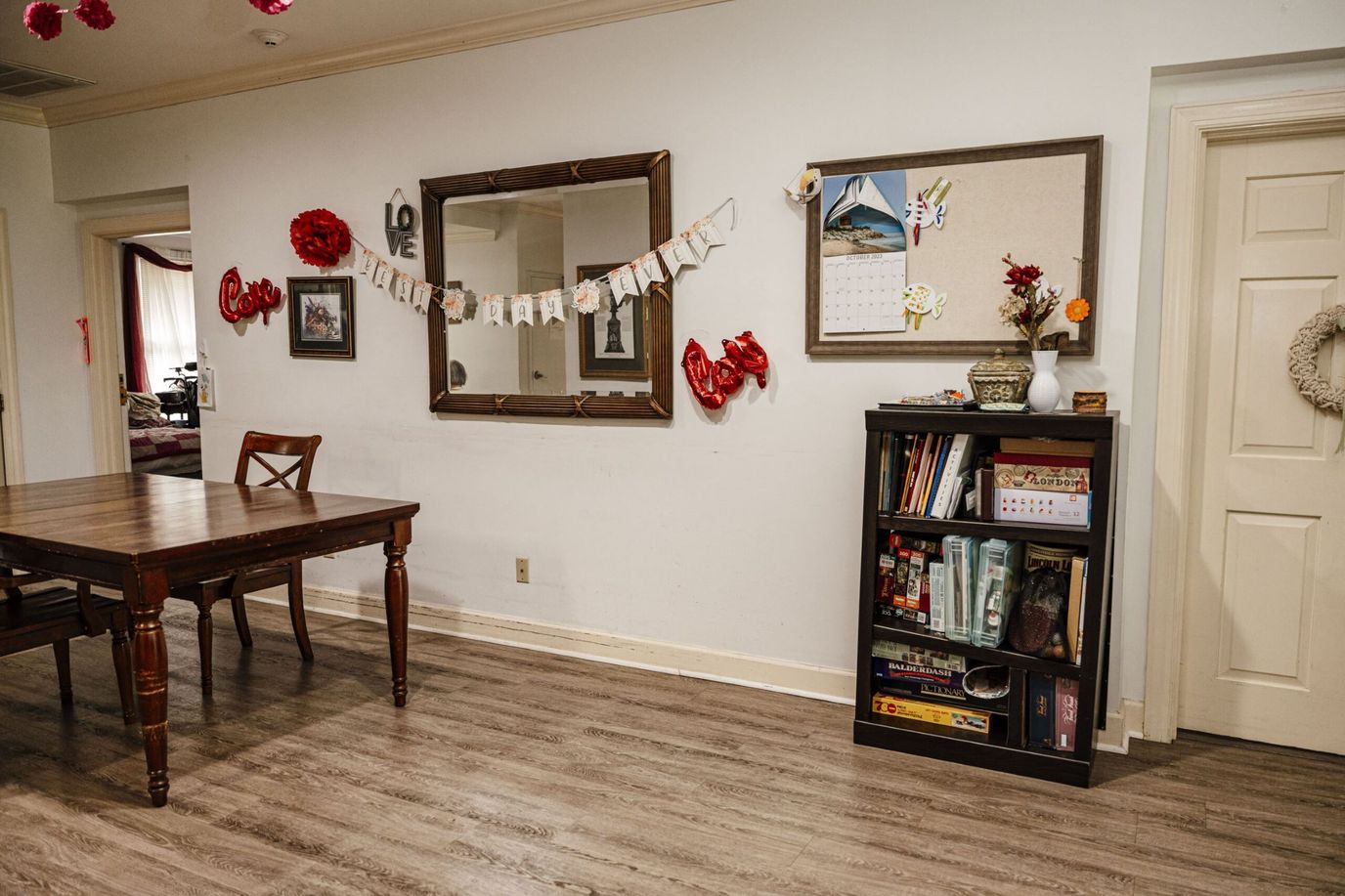 Cozy common area featuring a wooden table, a mirror, and a bookshelf filled with games and books.
