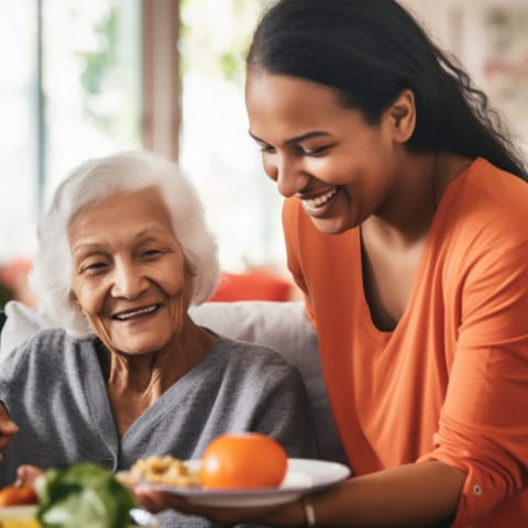 A caregiver serving food to a smiling elderly resident