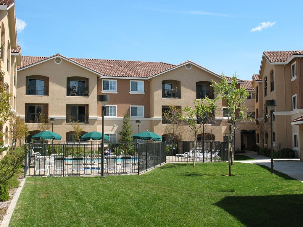 Swimming pool area with lounge chairs and umbrellas at Vintage Zinfandel Senior Apartments.