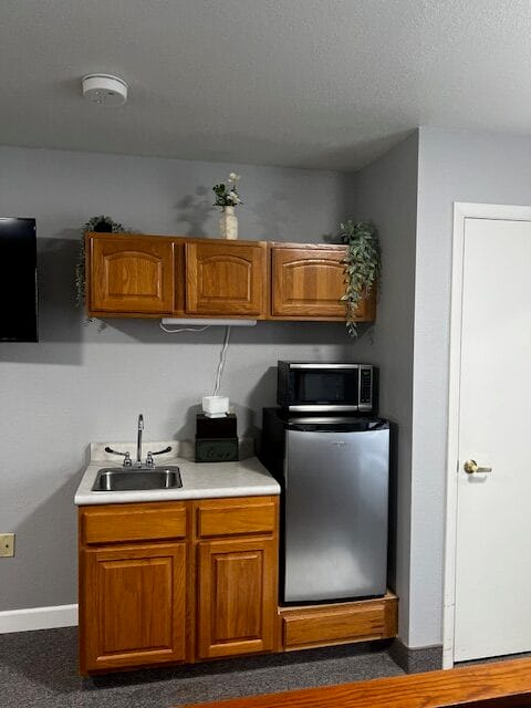 A kitchenette featuring wooden cabinets, a sink, a microwave, and a small refrigerator.