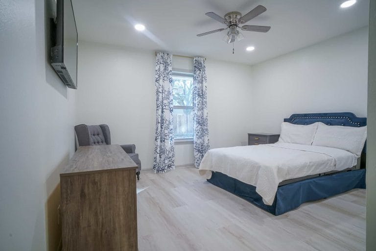 A cozy bedroom with a bed, dresser, and armchair.
