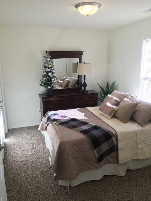 A cozy bedroom with a bed, dresser, and small Christmas tree.