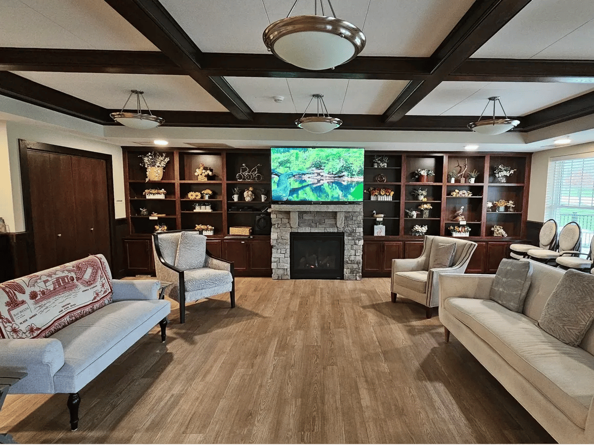 A cozy living room with a stone fireplace, comfortable seating, and a TV displaying nature scenery.