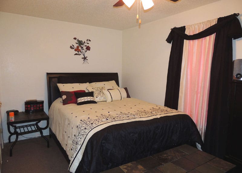 A neatly arranged bedroom featuring a bed with decorative pillows, a bedside table, and curtains.