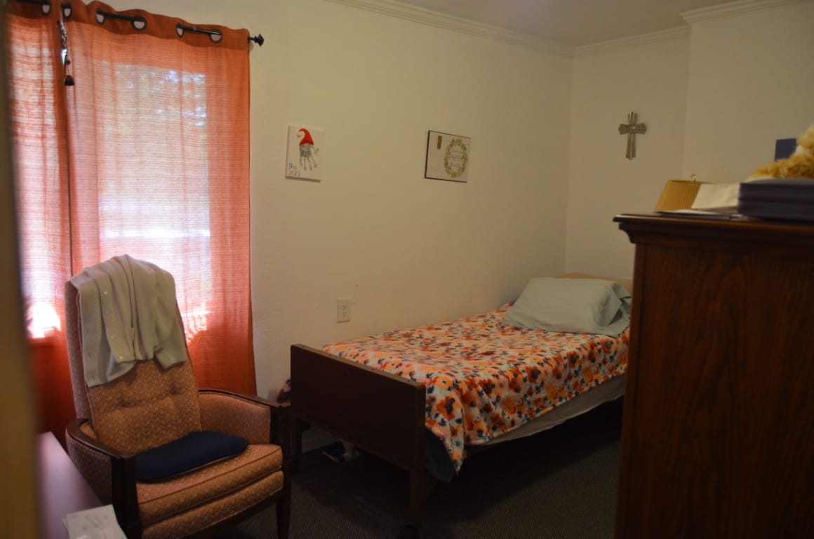 A simple bedroom with a bed, armchair, and window curtains.