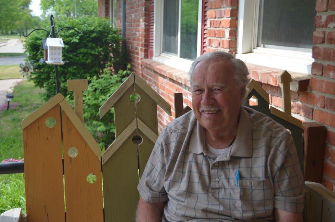 Smiling senior man sitting on a colorful bench on the porch