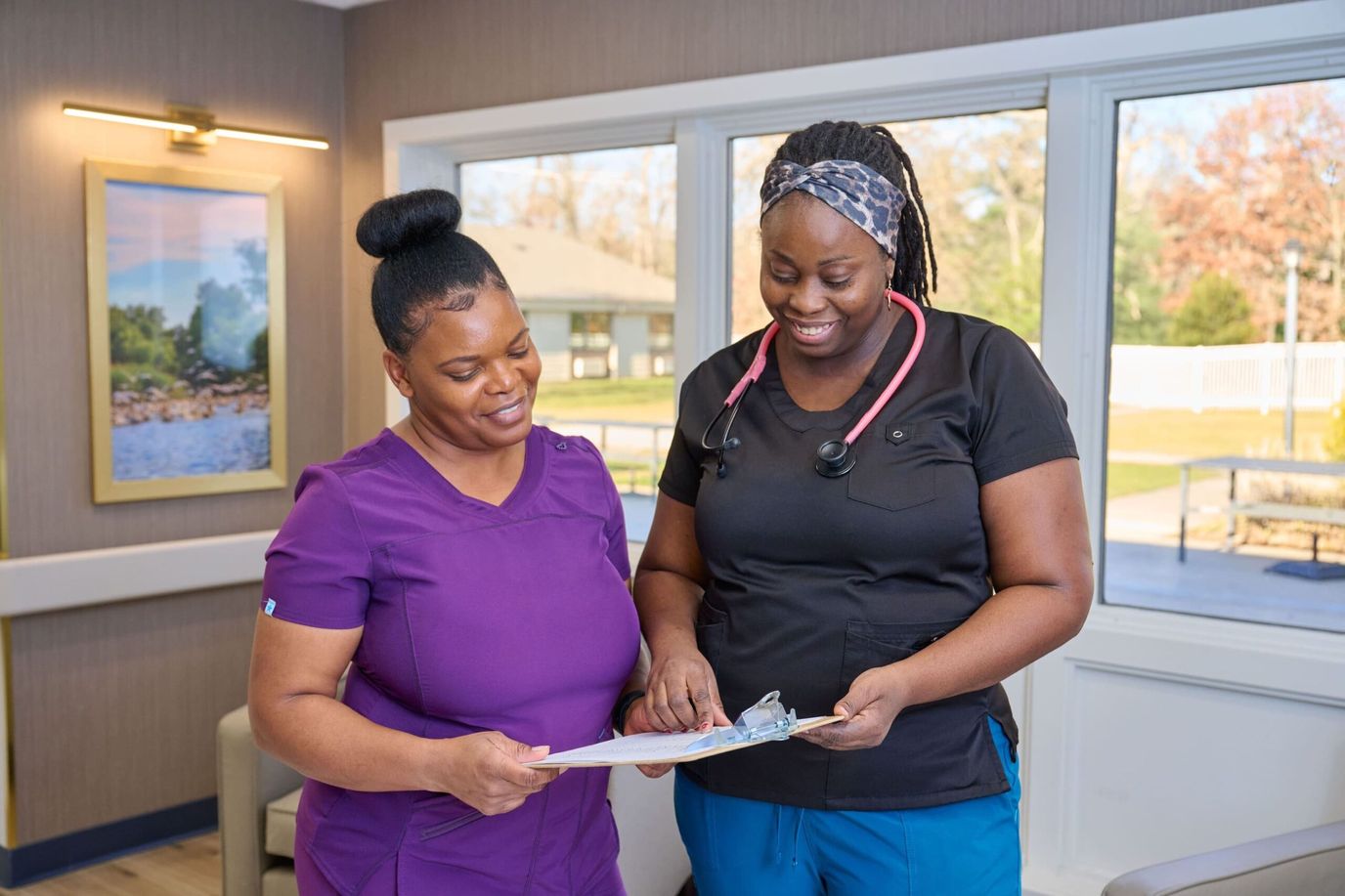 Two caregivers discussing a clipboard in a bright lounge area