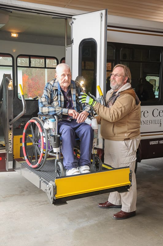 Staff assisting a resident in a wheelchair at the facility van