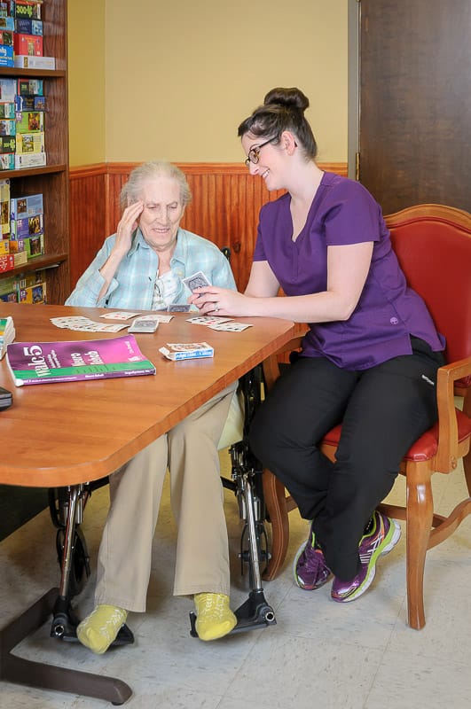 Resident and staff member playing cards in an activity room