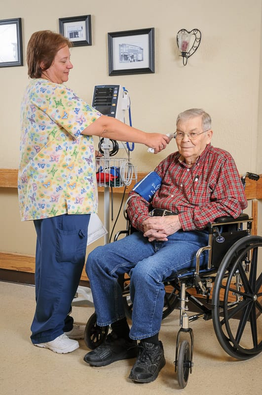 Staff member taking a resident's vital signs in a room