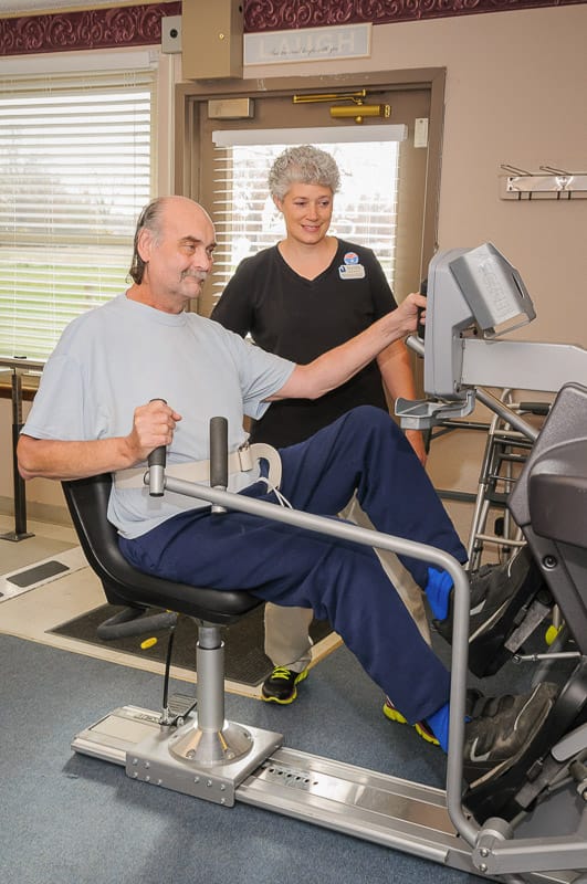 Resident using an exercise machine with staff assistance
