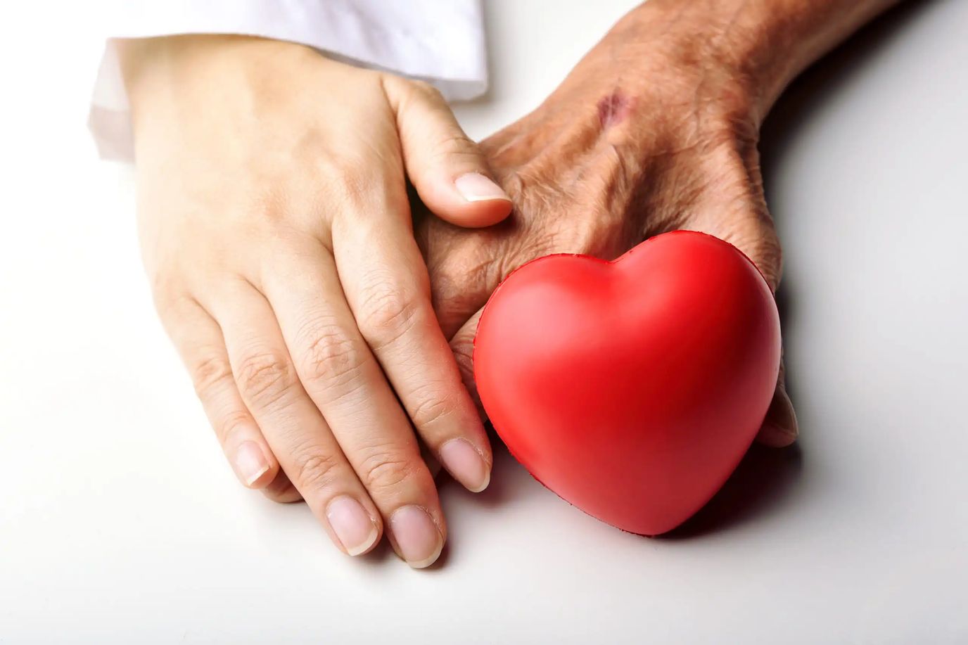 A caregiver's hand holding a senior's hand with a heart