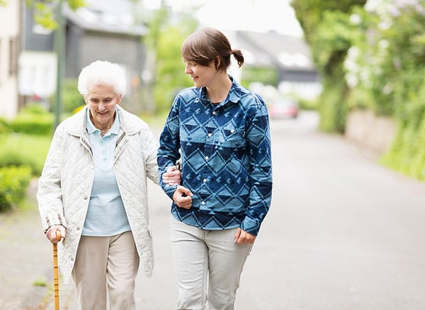A caregiver assisting an elderly woman on a path