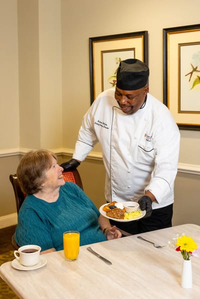 A dining scene with a chef serving food to a resident