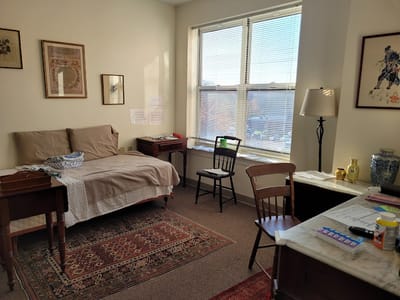 A well-lit resident room with a bed and writing desk