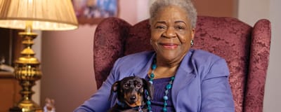 Senior woman holding a small dog in a cozy chair.