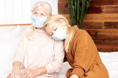 Two women wearing masks in a cozy indoor setting