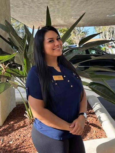 Staff member posing outdoors near plants.