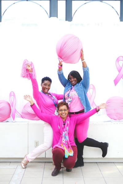 Three staff members celebrating with pink decorations