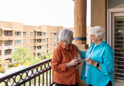 Two residents enjoying drinks on a balcony at the facility