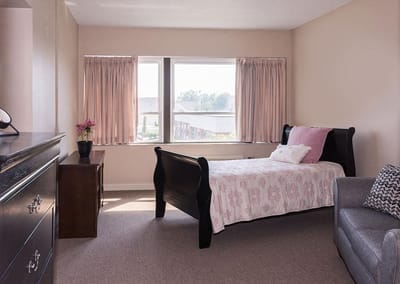 Well-lit private resident room with bed and furniture