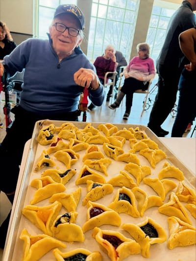 Resident preparing trays of hamantaschen pastries with smiles.