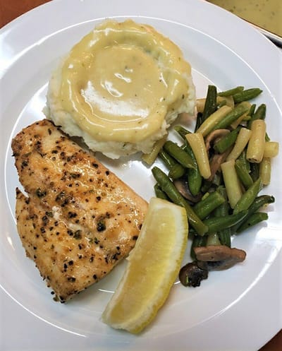 A plated meal featuring fish, mashed potatoes, and green beans