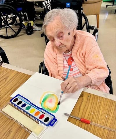 An elderly woman painting in an activity room