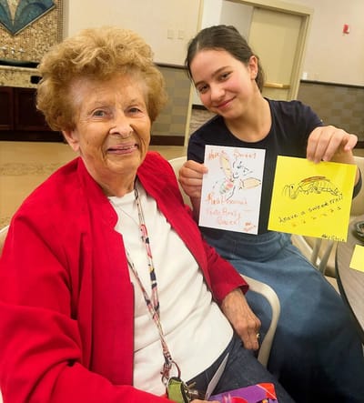 A resident and a child displaying handmade drawings together