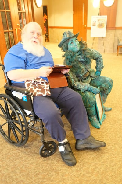 A resident in a wheelchair with a performer in costume in a common area.