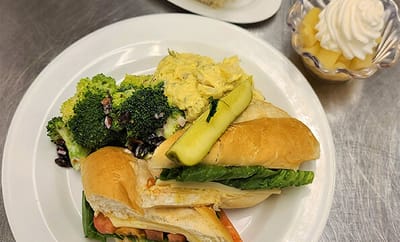 A plated meal featuring a sandwich, broccoli, and dessert.