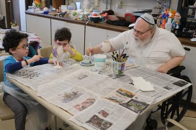 An elderly man painting with two children at a table