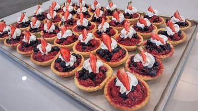 A tray of colorful fruit tarts topped with cream