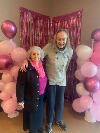 Two residents smiling at a celebration with pink decorations